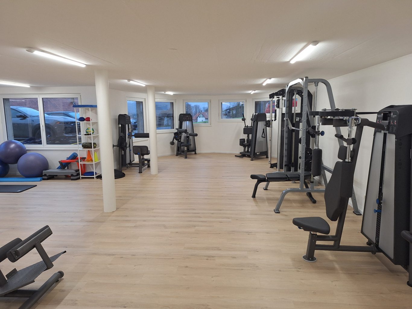 Fitnessraum mit Geräten, freien Gewichten und großen Fenstern für natürliches Licht.