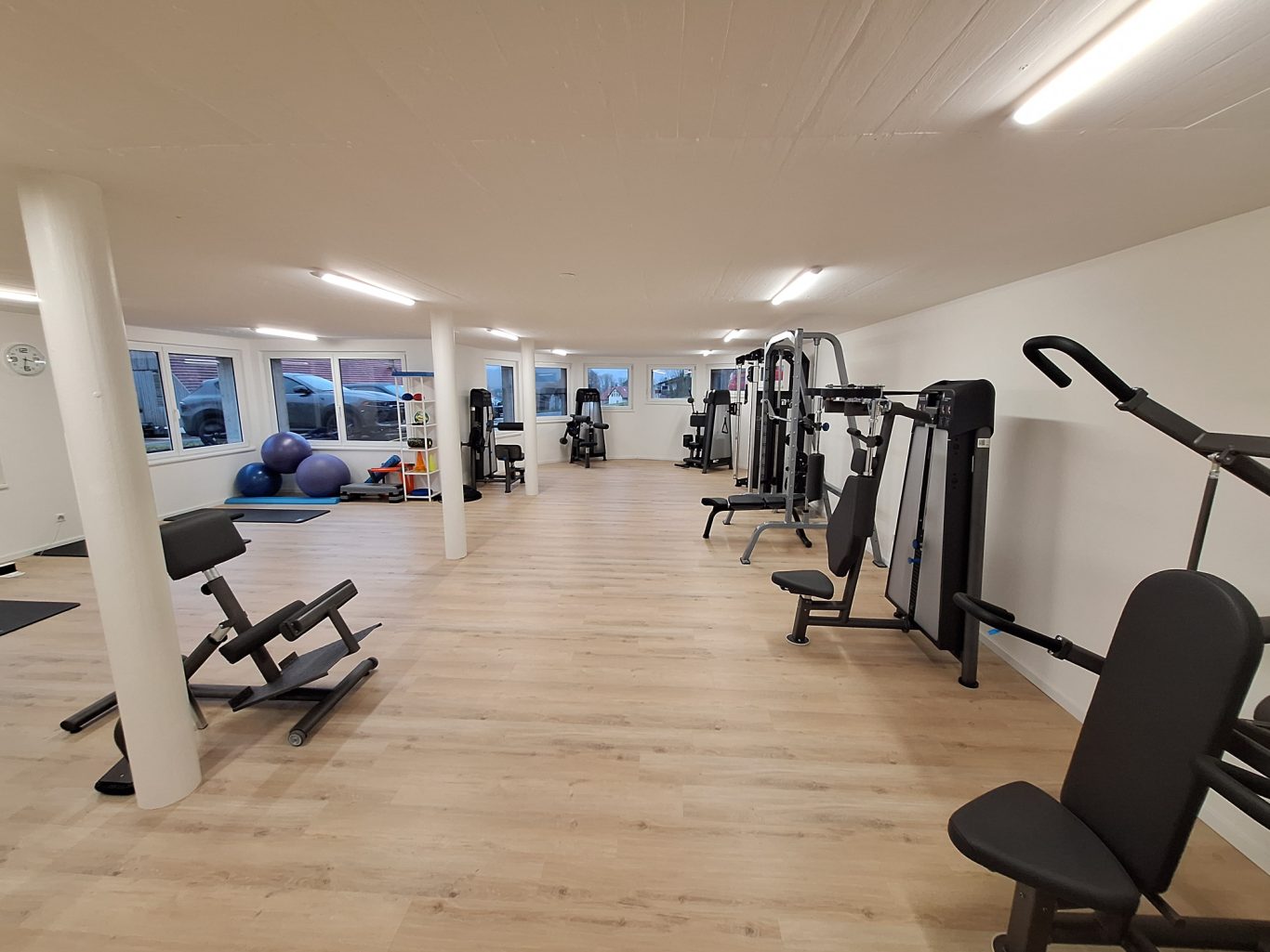 Fitnessraum mit verschiedenen Trainingsgeräten und Fenstern für natürliches Licht.
