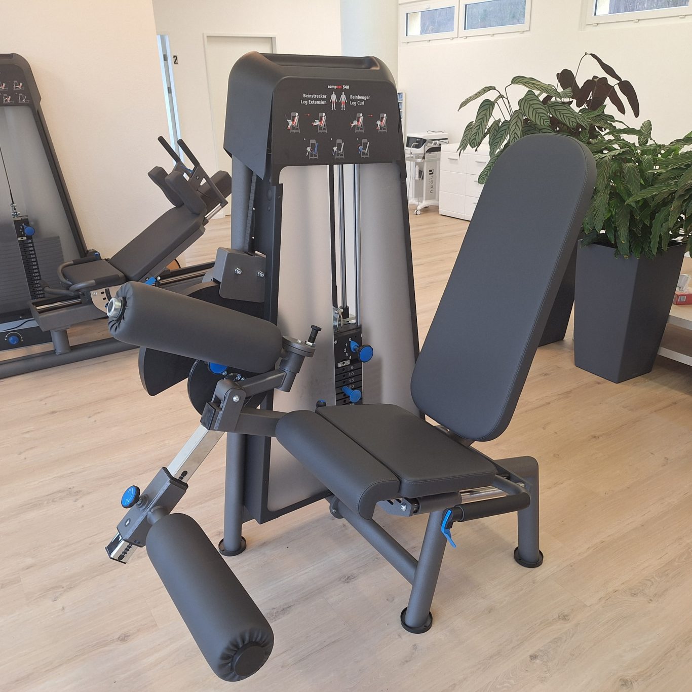 Krafttrainingsgerät mit verstellbarem Sitz und Beinstütz in modernem Fitnessstudio.
